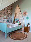 Child's bed with canopy, floral wallpaper and wooden bedside table in the nursery