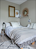 Bedroom with bed, rattan mirror and picture frame on beige wall