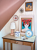 Decorative side table with lamp, picture, porcelain boxes and porcelain plate under sloping roof