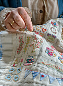 Nahaufnahme einer Hand beim Sticken eines bunten Patchwork-Quilts