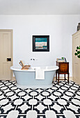 Freestanding, light blue bathtub on patterned tiles with side table