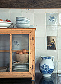 Wooden display cabinet with ceramic bowls and eggs in front of a white tiled wall