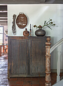 Antique wooden cabinet with rustic decorative objects in hallway with tiled floor