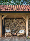 Covered woodpile area with two rattan armchairs and small side table