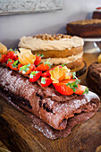 Chocolate sponge roll with strawberries and physalis on a wooden plate