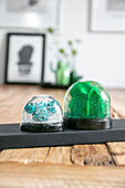 DIY snow globes with green and blue glitter elements on wooden table