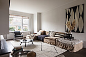 Living room in natural tones with L-shaped sofa and geometric mural