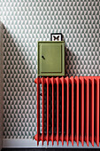 Red radiator and green key box in front of geometrically patterned wallpaper
