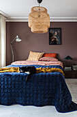 Bedroom with rattan pendant light and cat lying on dark blue bedspread