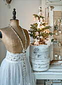 Alte Schneiderpuppe mit Perlenkette und mit spitzenbesetztem Kleidungsstück, dahinter  Weihnachtsbäumchen mit Baumwollpuppen geschmückt