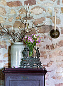 Antique vases with flowers and magnolia branches on wooden cabinet in front of natural stone wall
