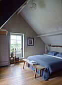 Double bed with blue linen ceiling and wooden bench in the attic bedroom with oak floorboards