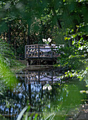 Wooden terrace with table and chairs on the banks of a tranquil pond in the garden