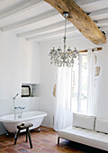 White, cozy bathroom with chandelier on rustic wooden beams