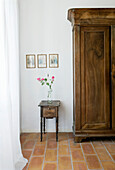 Wooden wardrobe, next to antique bedside table with flower and pictures on the wall