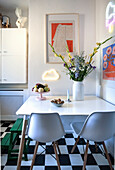 Cozy kitchen corner with white table, bouquet of flowers and pictures, floor in checkerboard pattern