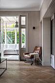 Hallway with herringbone parquet flooring, leather chair and view into the conservatory