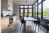 Modern kitchen with long dining table, black chairs and view of the garden