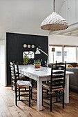 Dining area with white wooden table, black chairs and wicker lamp