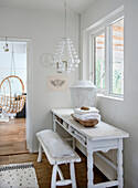 White console table with wooden bench and decoration, hanging chair in the background