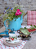 Summery garden table with flowers in a blue watering can and tea service