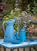 Blaue Vintage-Kannen mit blühenden Wildblumen auf Gartentisch