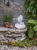 Bust on a stone pedestal, surrounded by various plants