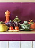 Ceramic crockery in the shape of vegetables on a shelf in front of a purple wall