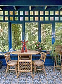 Rattan table and chairs in conservatory with plants and patterned tiled floor and wall of windows