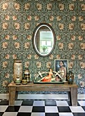 Vases, figurine and picture on wooden bench in front of patterned wallpaper in hallway