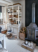 White country-style kitchen shelf next to antique wood-burning stove, cat in wooden box