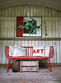 Red metal bench with decorative pillows in front of a wooden wall in the garden shed