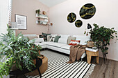 Wohnzimmer mit weißem Ecksofa, gestreiftem Teppich und Grünpflanzen