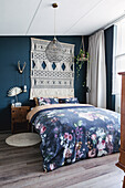 Bedroom with dark blue wall, macramé wall hanging and floral bed linen