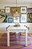 Dining room with white table, metal chairs, wicker lamp and picture gallery on the wall