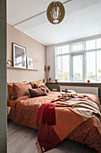 Bed with terracotta-coloured throw and cushions in modern bedroom