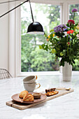 Pastries and bouquet of flowers on marble table in bright dining room