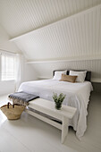 Bedroom in white with basket and bench at the end of the bed, sloping ceiling