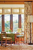 Bright dining area by the window with wooden furniture, green tablecloth and floral patterned curtains