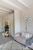 Open-plan living room with pink sofa, guitar and white ceiling beams