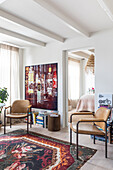 Living room with leather chairs, colorful carpet and piles of books