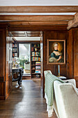 Wood-paneled living room with antique portrait and bookshelf in the background