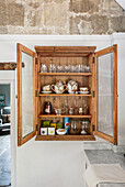 Hanging display cabinet with open doors filled with jugs, cups and glasses