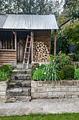 Garden beds with ornamental plants and firewood storage in front of garden shed