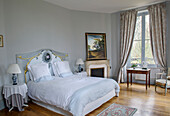 Double bed with ornate headboard next to the fireplace in the bedroom in soft blue tones