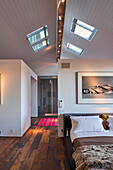 Double bed in front of room divider in bedroom with dark floorboards and skylights