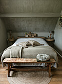 Bed with bed bench, natural colors and rustic decorative elements in bedroom with sloping roof