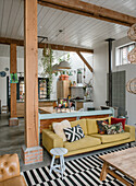 Open-plan living area with wooden beams, yellow sofa and striped carpet