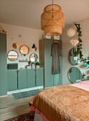 Bedroom with mint green wardrobes, rattan lamp and lots of mirrors