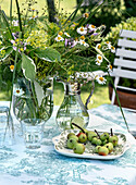 Glass vase and carafe with meadow flowers and plate with apples on a laid garden table